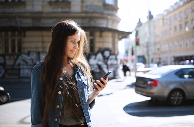 Woman standing in city using her cell phone (Unsplash)