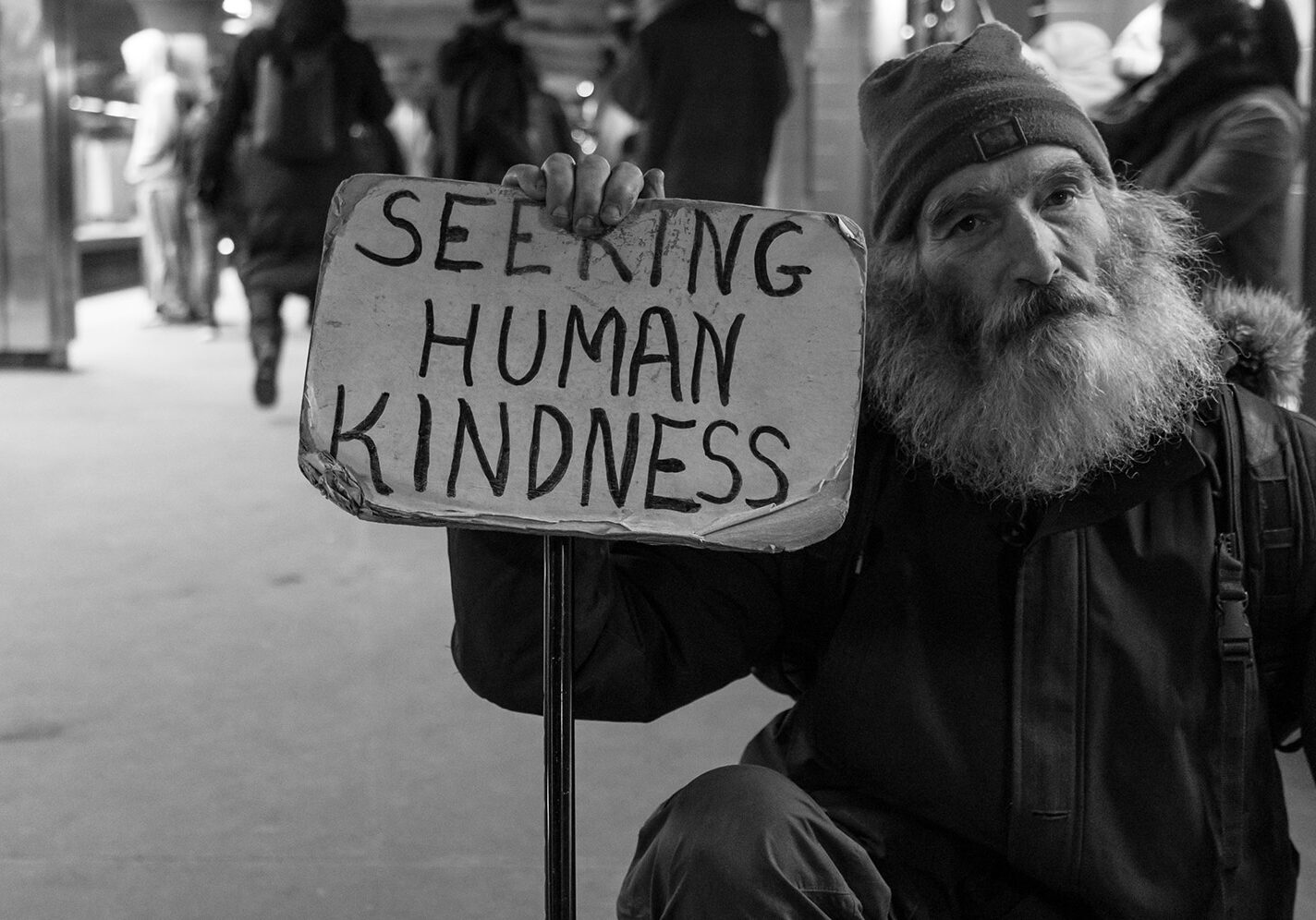 Man in bus station with human kindness sigh (Unsplash)