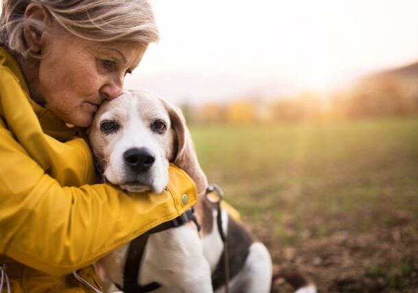 Woman in a yellow coat hugging her dog in a field (unsplash)